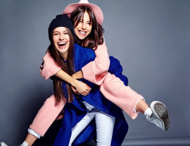 iki esmer bayan modelleri yaz casual hipster palto gri arka plan üzerinde poz içinde gülümseyen moda portre. Birbirlerine arkasında tutarak kızlar 