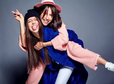 iki esmer bayan modelleri yaz casual hipster palto gri arka plan üzerinde poz içinde gülümseyen moda portre. Birbirlerine arkasında tutarak kızlar 