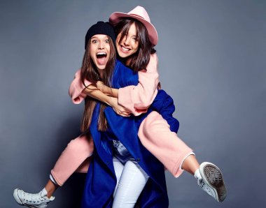 iki esmer bayan modelleri yaz casual hipster palto gri arka plan üzerinde poz içinde gülümseyen moda portre. Birbirlerine arkasında tutarak kızlar 