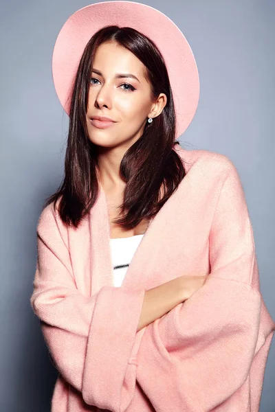 Beautiful smiling hipster brunette woman model in stylish pink overcoat and colorful hat posing on gray background — Stock Photo, Image