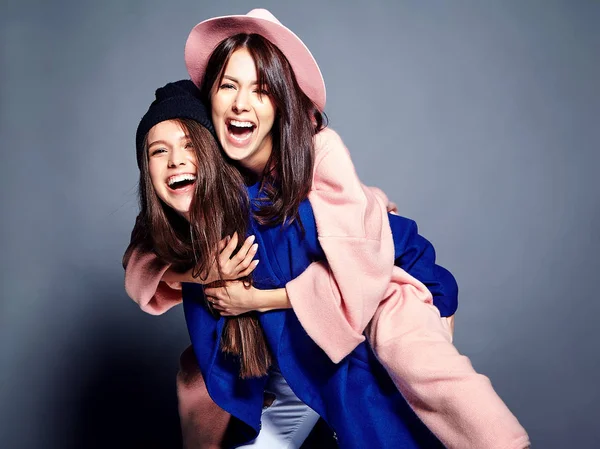 iki esmer bayan modelleri yaz casual hipster palto gri arka plan üzerinde poz içinde gülümseyen moda portre. Birbirlerine arkasında tutarak kızlar 