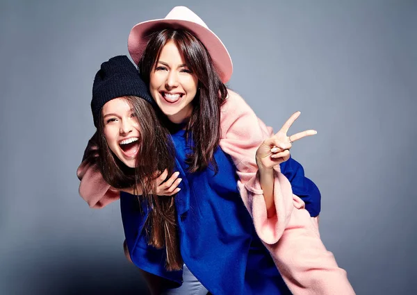 iki esmer bayan modelleri yaz casual hipster palto gri arka plan üzerinde poz içinde gülümseyen moda portre. Birbirlerine arkasında tutarak kızlar 