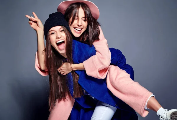 Mode Porträtt av två leende brunett kvinnor modeller i sommar casual hipster överrock poserar på grå bakgrund. Flickor som håller varandra om ryggen — Stockfoto