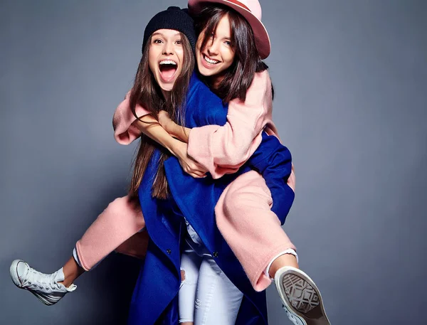 Retrato de moda de dos mujeres morenas sonrientes modelos en verano abrigo hipster casual posando sobre fondo gris. Chicas abrazándose en la espalda —  Fotos de Stock