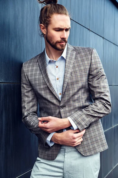 portrait of sexy handsome fashion male model man dressed in elegant checkered suit posing outdoors on the street background