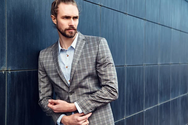 portrait of sexy handsome fashion male model man dressed in elegant checkered suit posing outdoors on the street background