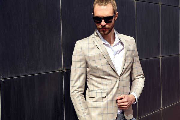 portrait of sexy handsome fashion male model man dressed in elegant checkered suit posing outdoors on the street background