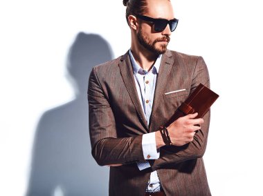 yakışıklı şık hipster işadamı manken portresi Studio beyaz duvarının yakınında poz güneş gözlüklü zarif kahverengi takım elbise giymiş. Çıkarır veya onun deri cüzdan ceket cebine attı