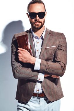 yakışıklı şık hipster işadamı manken portresi Studio beyaz duvarının yakınında poz güneş gözlüklü zarif kahverengi takım elbise giymiş. Çıkarır veya onun deri cüzdan ceket cebine attı
