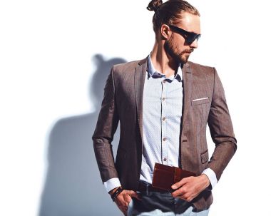 yakışıklı şık hipster işadamı manken portresi Studio beyaz duvarının yakınında poz güneş gözlüklü zarif kahverengi takım elbise giymiş. Çıkarır veya onun deri cüzdan ceket cebine attı