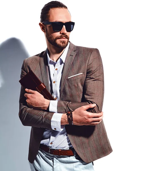 Retrato de moda elegante modelo de homem de negócios hipster elegante vestido com terno marrom elegante em óculos de sol posando perto da parede branca em estúdio. Puxa para fora ou colocar sua carteira de couro no bolso do casaco — Fotografia de Stock