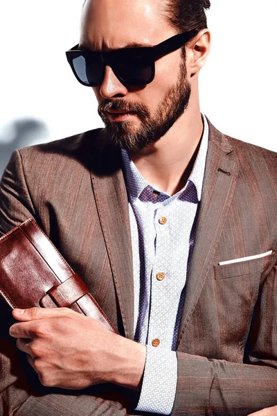 Retrato de moda atractiva modelo hipster hombre de negocios elegante vestido con traje marrón elegante en gafas de sol posando cerca de la pared blanca en el estudio. Saca o pone su billetera de cuero en el bolsillo de la chaqueta —  Fotos de Stock