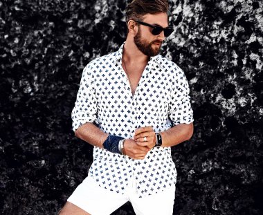 Portre yakışıklı moda giyen adam model beyaz elbise yakınındaki plajda kayalar poz