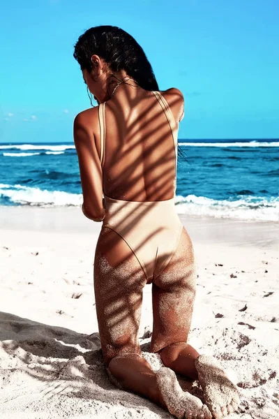 Gyönyörű kaukázusi napfürdette nő portréja bézs fürdőruha pózol a nyári strand, fehér homok, kék ég és az óceán háttér-sötét hosszú hajú modell. Palm árnyékok — Stock Fotó