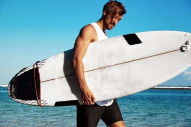 Moda erkek modeli sörfçü surfboard ile gidiş mavi okyanus ve gökyüzü arka plan rahat kıyafetler giymiş yakışıklı hipster portresi sunbathed