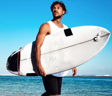 Moda erkek modeli sörfçü surfboard ile gidiş mavi okyanus ve gökyüzü arka plan rahat kıyafetler giymiş yakışıklı hipster portresi sunbathed