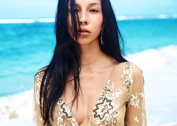 Sensual portrait of beautiful caucasian woman model with dark long hair in beige blouse posing on summer beach with white sand on blue sky and ocean background — Stock Photo, Image