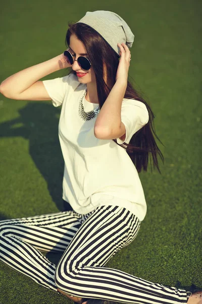 Fashion stylish beautiful young brunette woman model in summer hipster casual clothes posing on street background in the park — Stock Photo, Image