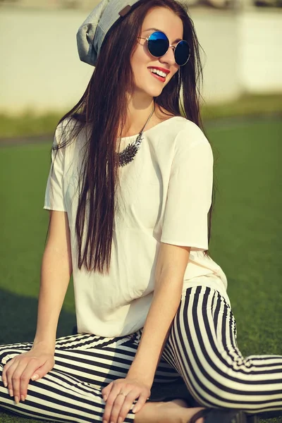 Fashion stylish beautiful young brunette woman model in summer hipster casual clothes posing on street background in the park — Stock Photo, Image