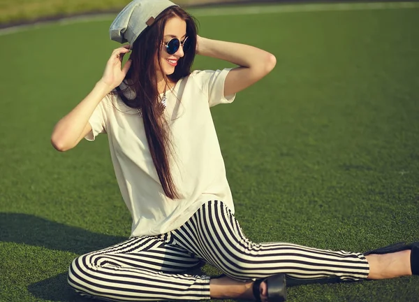 Fashion stylish beautiful young brunette woman model in summer hipster casual clothes posing on street background in the park — Stock Photo, Image