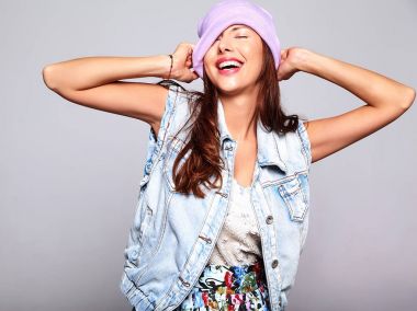 Güzel gülümseyen şirin esmer kadın modeli rahat yaz kot giysileri üzerinde gri izole mor beanie hiç makyaj ile portresi