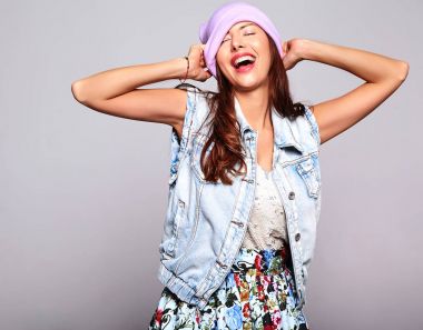 Güzel gülümseyen şirin esmer kadın modeli rahat yaz kot giysileri üzerinde gri izole mor beanie hiç makyaj ile portresi