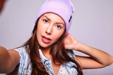 Mor beanie smartphone üzerinde gri izole selfie fotoğraf yapma hiç makyaj ile rahat yaz kot giysileri güzel şirin esmer kadın modeli portresi