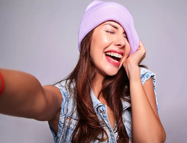 紫ビーニー グレーに分離されたスマート フォンで Selfie 写真を作るにぴんとジーンズのカジュアルな夏服で美しいの笑顔かわいいブルネットの女性モデルのポートレート — ストック写真