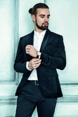 yakışıklı moda şık hipster lumbersexual işadamı modelinin portre Studio ışık mavi duvarının yakınında poz içinde zarif siyah takım elbise giymiş. Metroseksüel