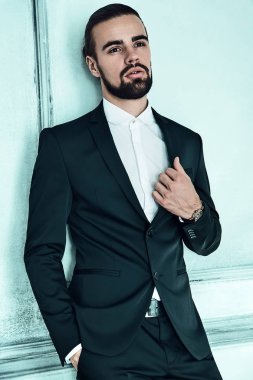 yakışıklı moda şık hipster lumbersexual işadamı modelinin portre Studio ışık mavi duvarının yakınında poz içinde zarif siyah takım elbise giymiş. Metroseksüel