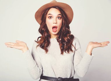 Karşılaştırma kavramı. Genç esmer kadın rahat kıyafetler ve bir ürün, benzer seçimi için düz iki elle görüntülemek kahverengi şapka gri arka plan stüdyo