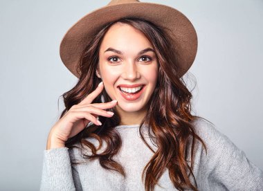 Genç şık gülen kız modeli gri rahat yaz giysileri ile doğal makyaj gri arka plan üzerinde izole kahverengi şapkalı portresi. Kameraya bakarak