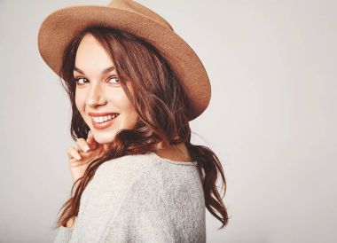 Genç şık gülen kız modeli gri rahat yaz giysileri ile doğal makyaj gri arka plan üzerinde izole kahverengi şapkalı portresi. Kameraya bakarak