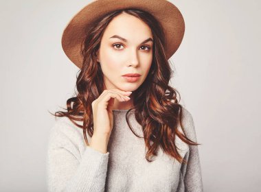 Şık çekici kadın modeli yatay portre Studio gri arka plan üzerinde poz doğal makyaj ile yaz giysileri ve kahverengi şapka takıyor. Kameraya bakarak