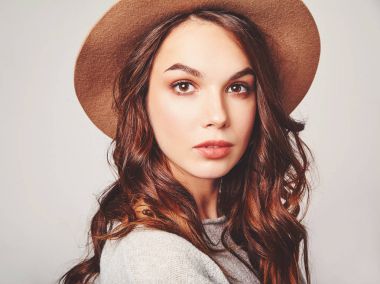 Şık çekici kadın modeli yatay portre Studio gri arka plan üzerinde poz doğal makyaj ile yaz giysileri ve kahverengi şapka takıyor. Kameraya bakarak