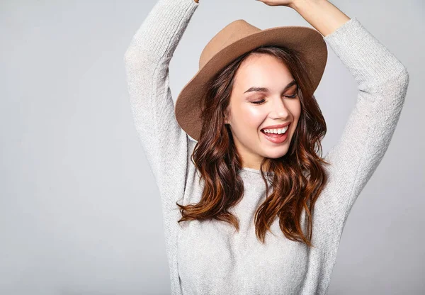 Genç şık gülen kız modeli gri rahat yaz giysileri ile doğal makyaj gri arka plan üzerinde izole kahverengi şapkalı portresi. Kameraya bakarak