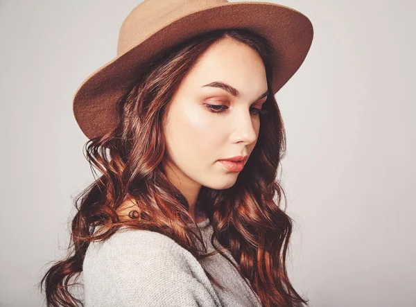 Şık çekici kadın modeli yatay portre Studio gri arka plan üzerinde poz doğal makyaj ile yaz giysileri ve kahverengi şapka takıyor. Kameraya bakarak