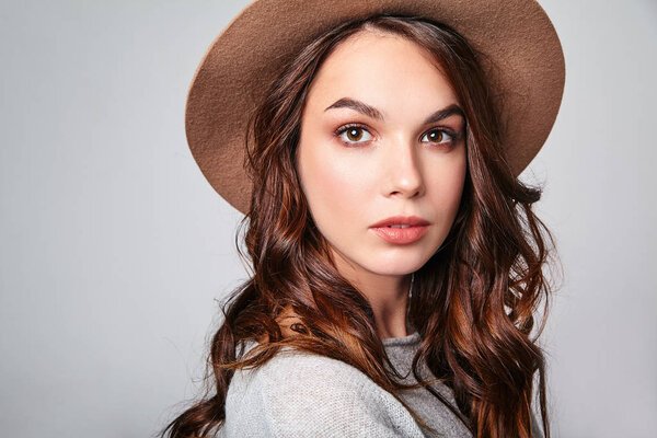 Horizontal portrait of stylish attractive female model wears summer clothes and brown hat with natural makeup posing on gray background in studio. Looking at camera