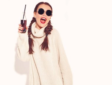 Genç mutlu gülümseyen kadın modeli ile parlak makyaj ve yaz sıcak kazak giysiler ve güneş gözlüğü üzerinde beyaz izole iki boynuzlu kırmızı dudaklar. Saman ile cam şişe soda içme
