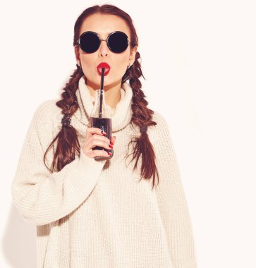 Genç mutlu gülümseyen kadın modeli ile parlak makyaj ve yaz sıcak kazak giysiler ve güneş gözlüğü üzerinde beyaz izole iki boynuzlu kırmızı dudaklar. Saman ile cam şişe soda içme