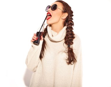 Genç mutlu gülümseyen kadın modeli ile parlak makyaj ve yaz sıcak kazak giysiler ve güneş gözlüğü üzerinde beyaz izole iki boynuzlu kırmızı dudaklar. İçme ve saman ile cam şişe soda yalama