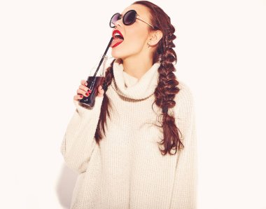 Genç mutlu gülümseyen kadın modeli ile parlak makyaj ve yaz sıcak kazak giysiler ve güneş gözlüğü üzerinde beyaz izole iki boynuzlu kırmızı dudaklar. İçme ve saman ile cam şişe soda yalama