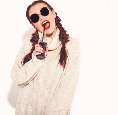 Genç mutlu gülümseyen kadın modeli ile parlak makyaj ve yaz sıcak kazak giysiler ve güneş gözlüğü üzerinde beyaz izole iki boynuzlu kırmızı dudaklar. Saman ile cam şişe soda içme