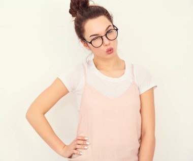 Genç güzel esmer kadın kız modeli renkli yaz pembe hipster giysileri duvara yakın poz çıplak makyaj ile portresi. Hava öpücük vererek ve göz kırpıyor