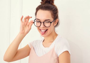 Genç güzel esmer kadın kız modeli renkli yaz pembe hipster giysileri duvara yakın poz çıplak makyaj ile portresi. Delirmek ve dilini gösteren