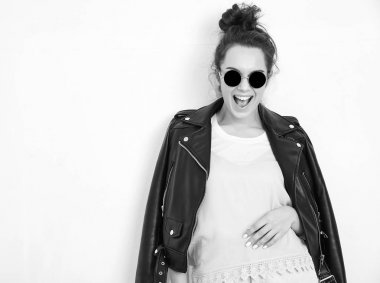 Genç güzel esmer kadın kız modeli ile çıplak makyaj duvara yakın poz güneş gözlüğü yaz hipster motorcu deri ceket elbise giyiyor portresi. Delirmek 