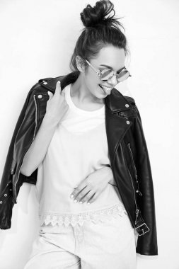 Genç güzel esmer kadın kız modeli ile çıplak makyaj duvara yakın poz güneş gözlüğü yaz hipster motorcu deri ceket elbise giyiyor portresi. Delirmek ve dilini gösteren