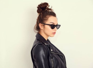 Genç güzel esmer kadın kız modeli ile çıplak makyaj duvara yakın poz güneş gözlüğü yaz hipster motorcu deri ceket elbise giyiyor portresi. Delirmek 