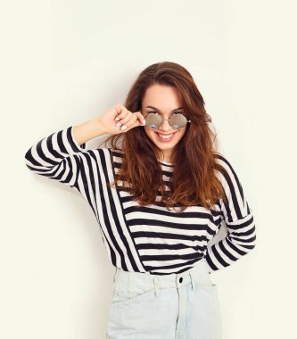 Genç güzel esmer kadın kız modeli yaz hipster giysiler ve güneş gözlüğü duvara yakın poz çıplak makyaj ile portresi. Delirmek 