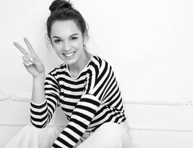 Genç güzel esmer kadın kız modeli yaz hipster giysileri duvara yakın poz çıplak makyaj ile portresi. Katta oturan ve barış işareti gösterilen